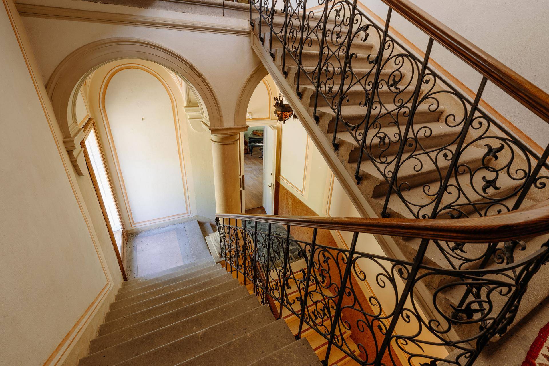 Historisches Treppenhaus mit schmiedeeisernem Geländer und gewölbten Durchgängen.