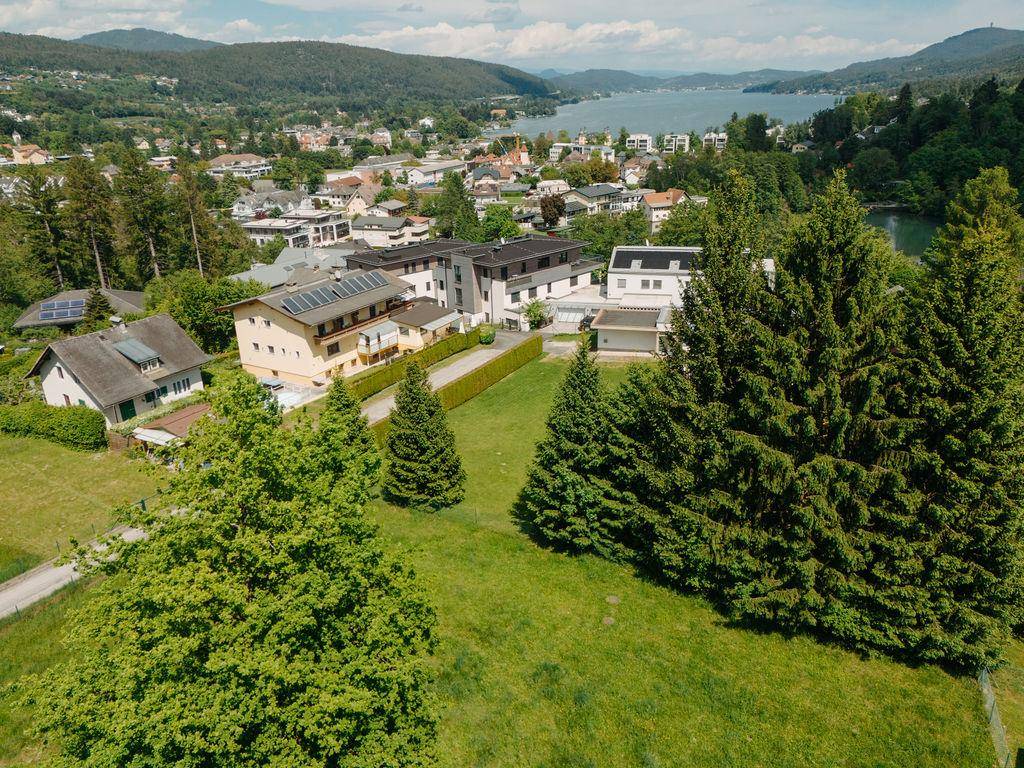Panoramablick auf ein Wohngebiet mit Häusern, viel Grün und einem See in der Ferne.