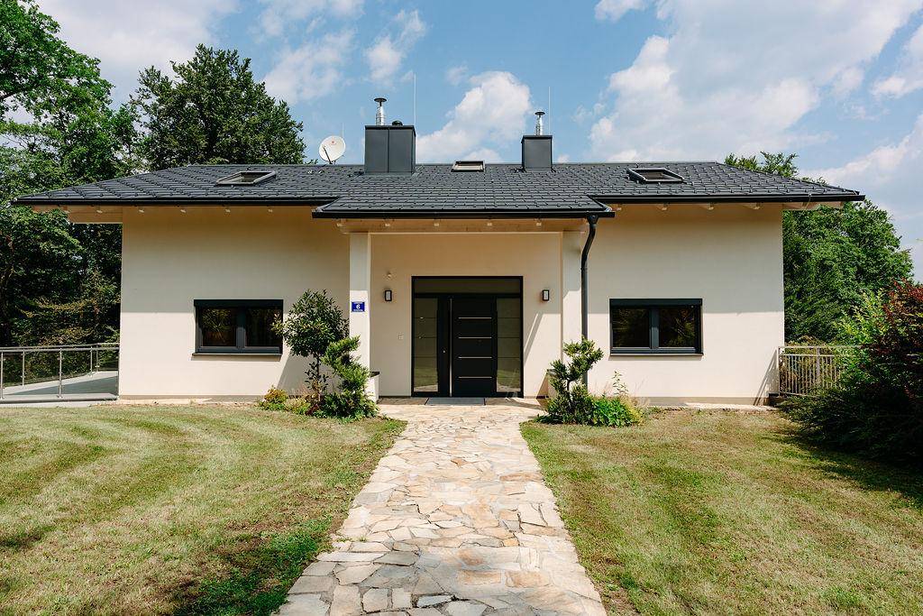 Moderne Hausfassade mit einladendem Eingangsbereich und gepflastertem Weg durch den Vorgarten.