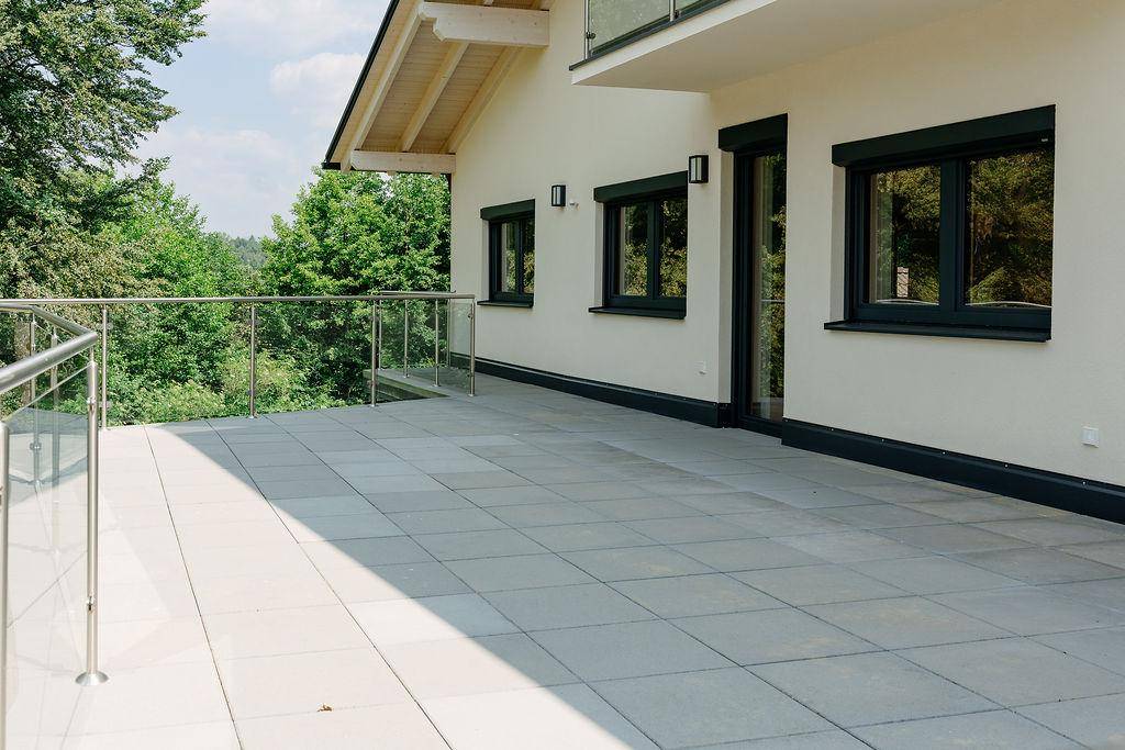 Geräumige, geflieste Terrasse mit modernem Glasgeländer und weitem Blick ins Grüne.
