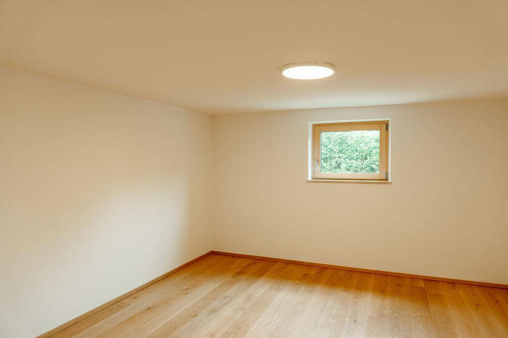 Helles Schlafzimmer mit Holzboden und Fenster mit Blick ins Grüne.