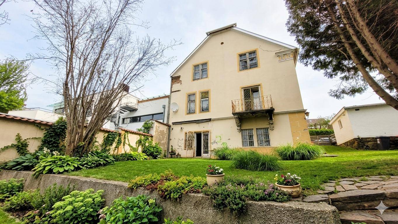 Altes Gebäude mit charmantem Gartenbereich, üppiger Bepflanzung und kleiner Terrasse.