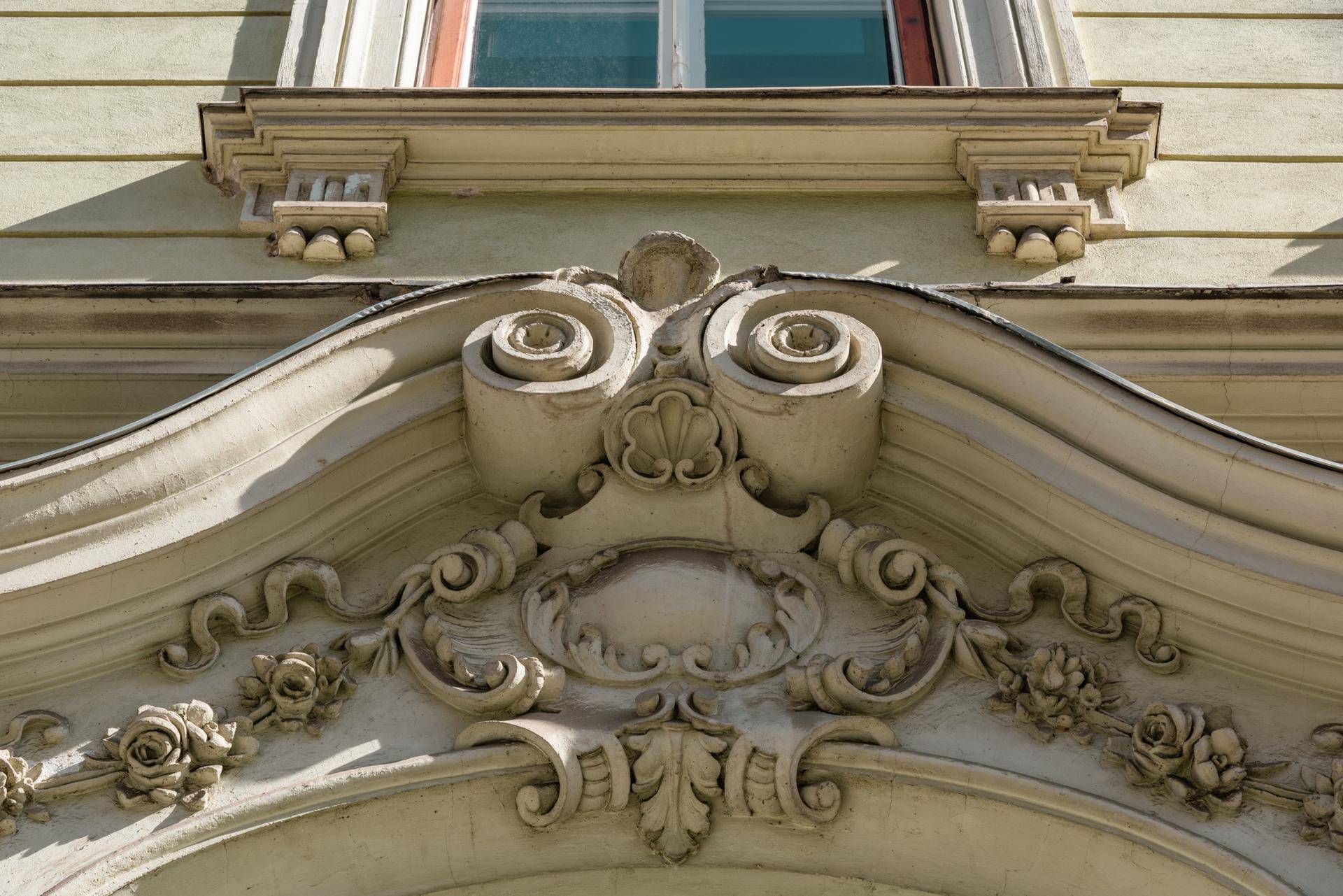 Nahaufnahme der kunstvollen Stuckverzierungen über dem Eingangsportal eines Altbaus.