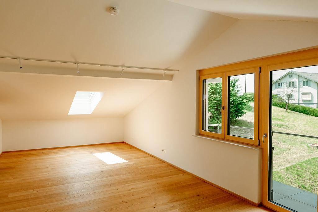 Geräumiges Schlafzimmer mit Holzboden, Dachschräge und Zugang zum Gartenbereich.