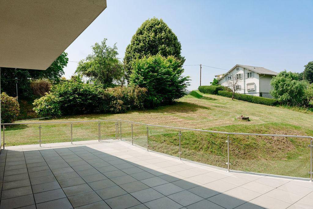 Leere Terrasse mit Glasgeländer und weitem Blick über die grüne Hügellandschaft.