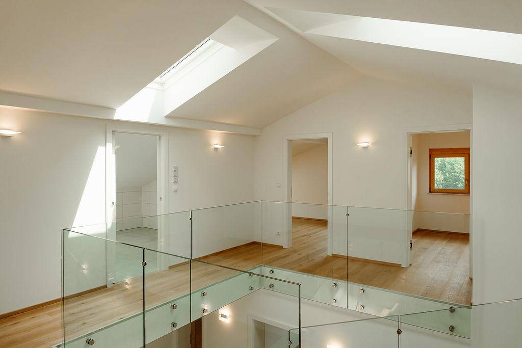 Heller Flur im Obergeschoss mit Glasgeländer und Dachfenster, das viel Licht spendet.