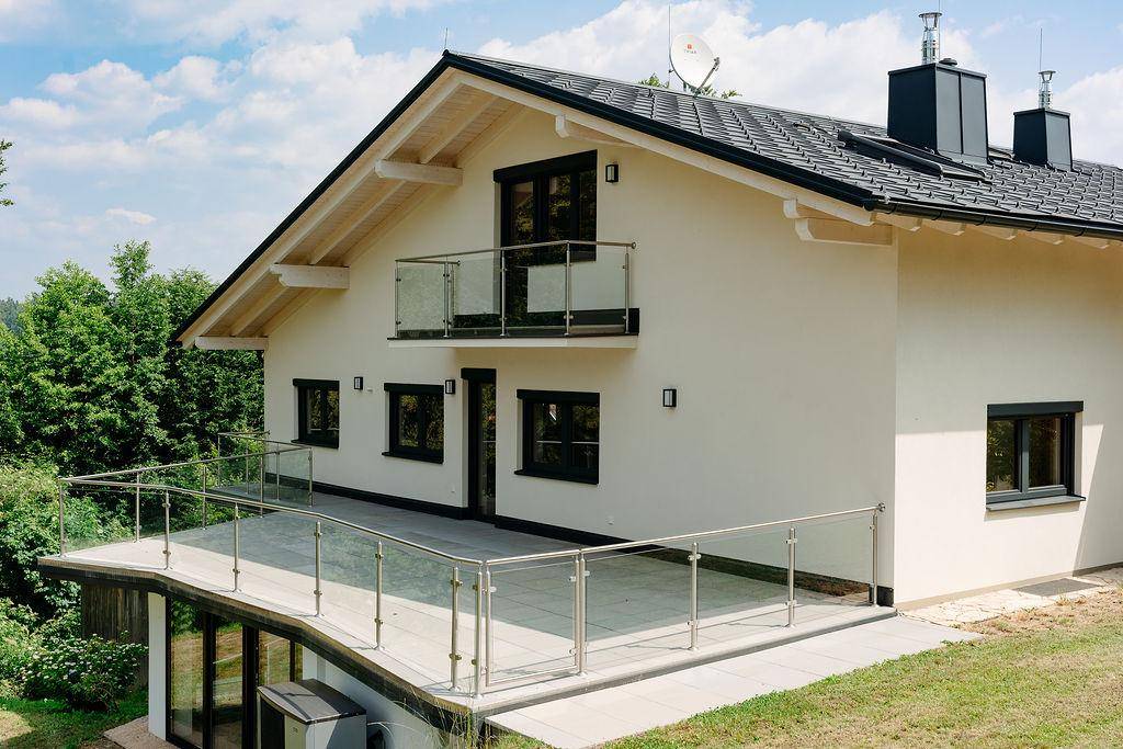 Geräumige Terrasse mit modernem Glasgeländer am Einfamilienhaus, umgeben von Natur.