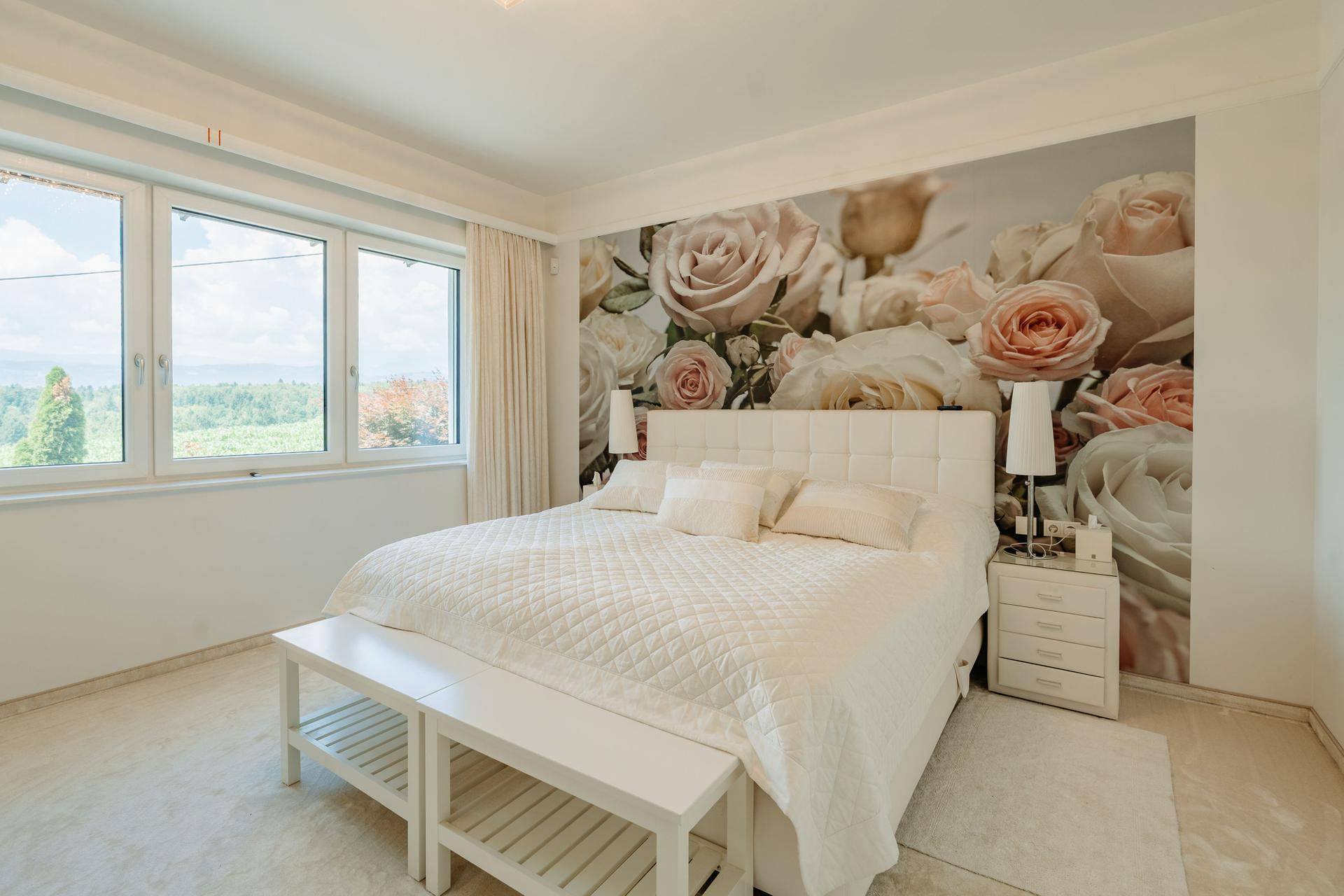 Gemütliches Schlafzimmer mit großem Doppelbett, floraler Tapete und weitem Blick aus den Fenstern.