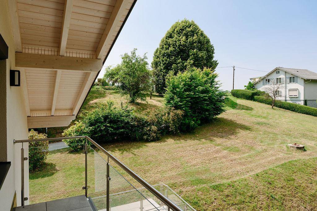 Balkon mit Glasgeländer und Blick auf die grüne Hügellandschaft und umliegende Häuser.