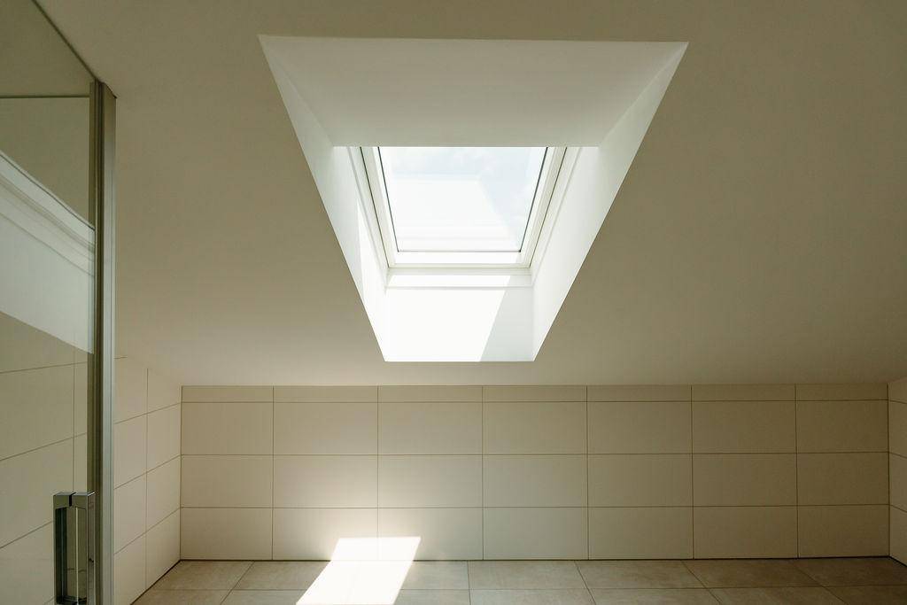 Modernes Badezimmer mit Dachfenster und hellen Fliesen, das viel Tageslicht hereinlässt.