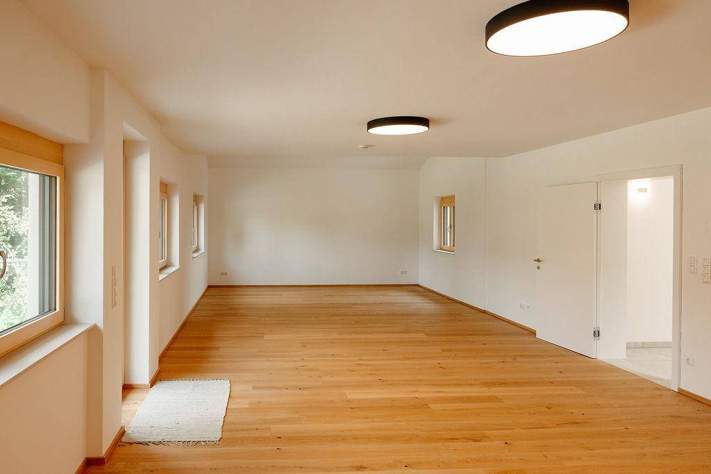 Helles, leeres Wohnzimmer mit Holzboden und großen Fenstern, bereit zur individuellen Einrichtung.