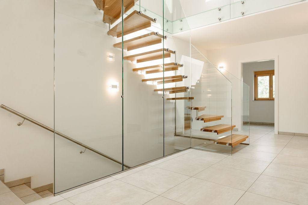 Heller Flur mit eleganter Holztreppe und Glasgeländer, die die Etagen stilvoll verbindet.