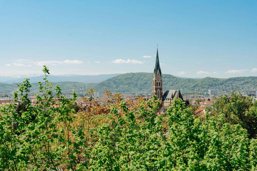 Klarer Blick auf den Kirchturm der Stadt, umgeben von grünen Bäumen und sanften Hügeln.