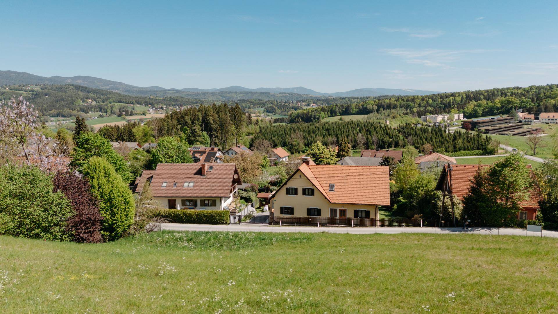 Idyllischer Ausblick auf eine Reihe von Wohnhäusern, eingebettet in eine grüne Landschaft mit Wäldern.