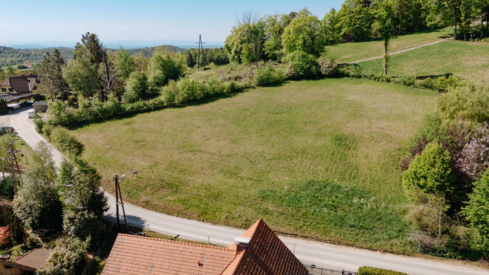 Weitläufiges Wiesengrundstück mit Blick auf bewaldete Hügel und eine Straße, umgeben von Natur.