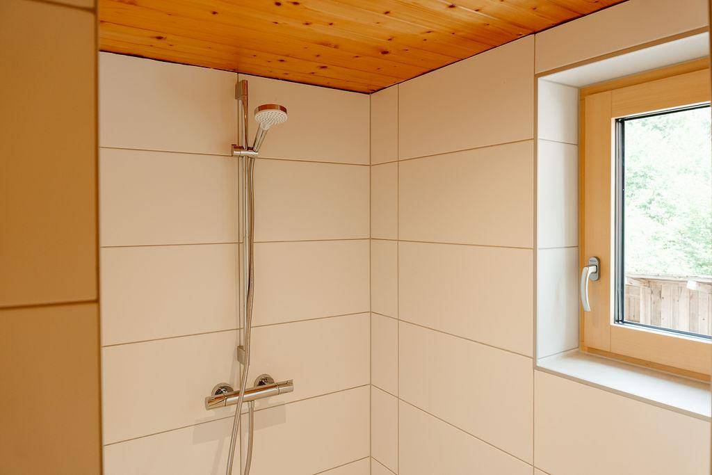 Duschbereich mit Holzdach und Fenster, hell gefliest, in einem modernen Badezimmer.