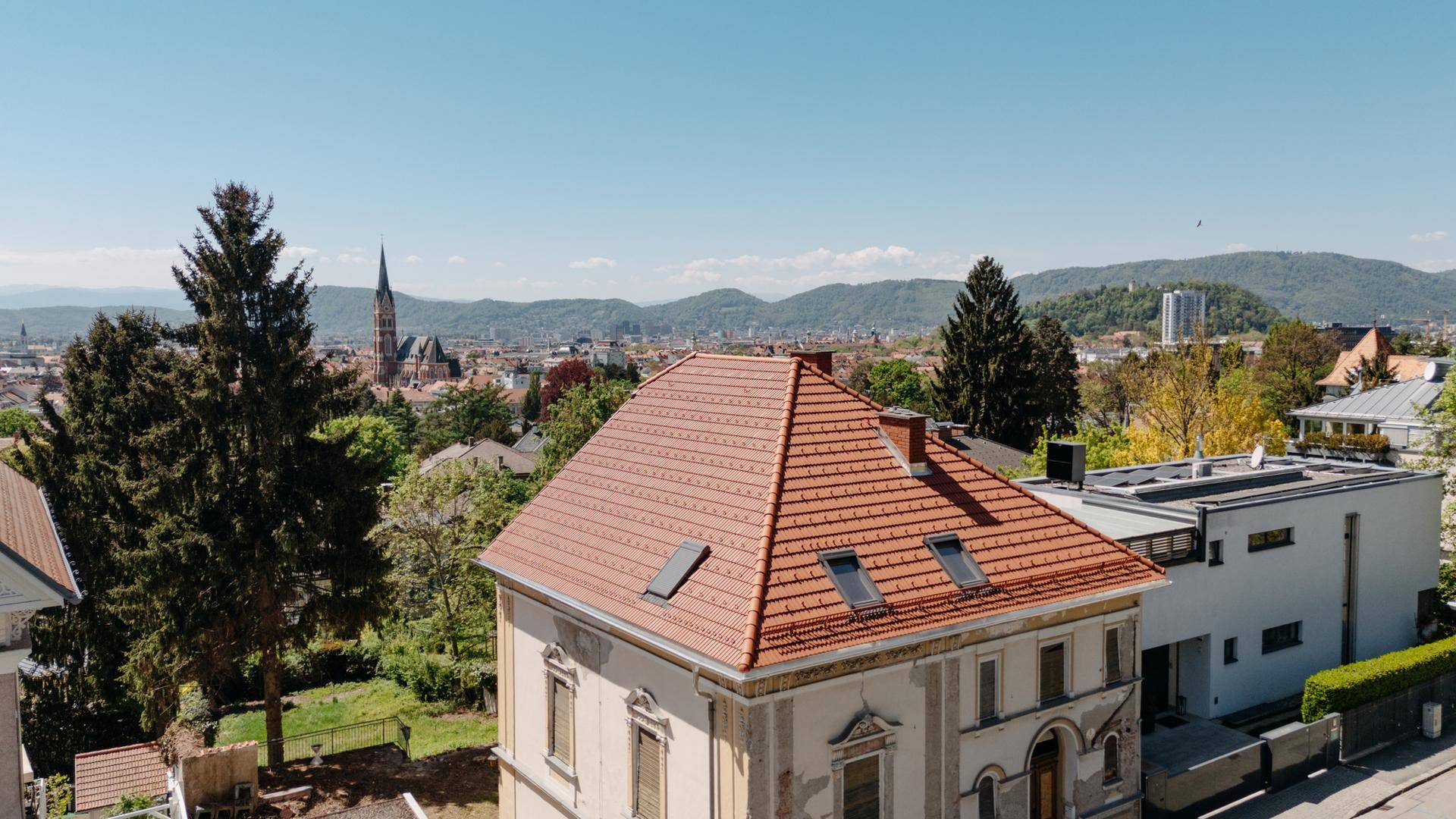 Historisches Gebäude mit neu gedecktem Ziegeldach, Dachfenstern und weitem Stadtblick.