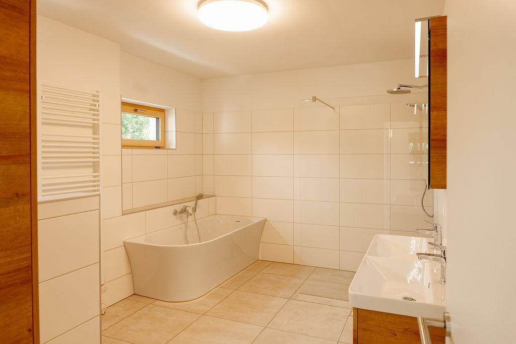 Helles Badezimmer mit freistehender Badewanne, Doppelwaschbecken und Fenster.