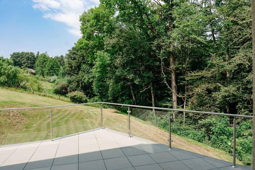 Ruhige Terrasse mit Glasgeländer und direktem Blick auf den angrenzenden Wald.