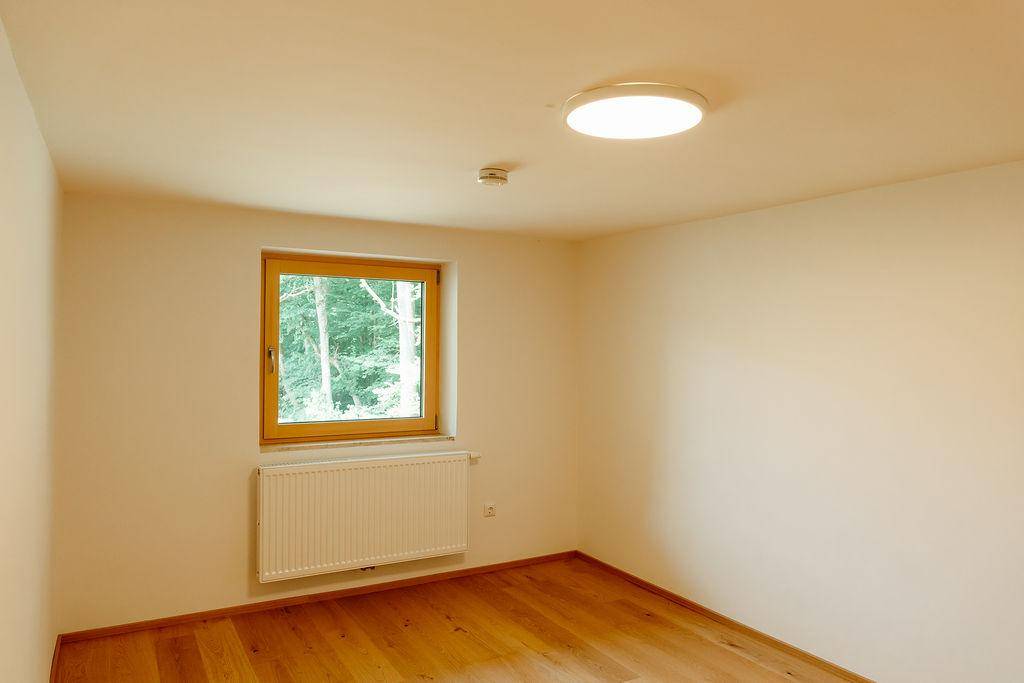 Helles Schlafzimmer mit Holzboden, Heizkörper und Fenster mit Blick ins Grüne.