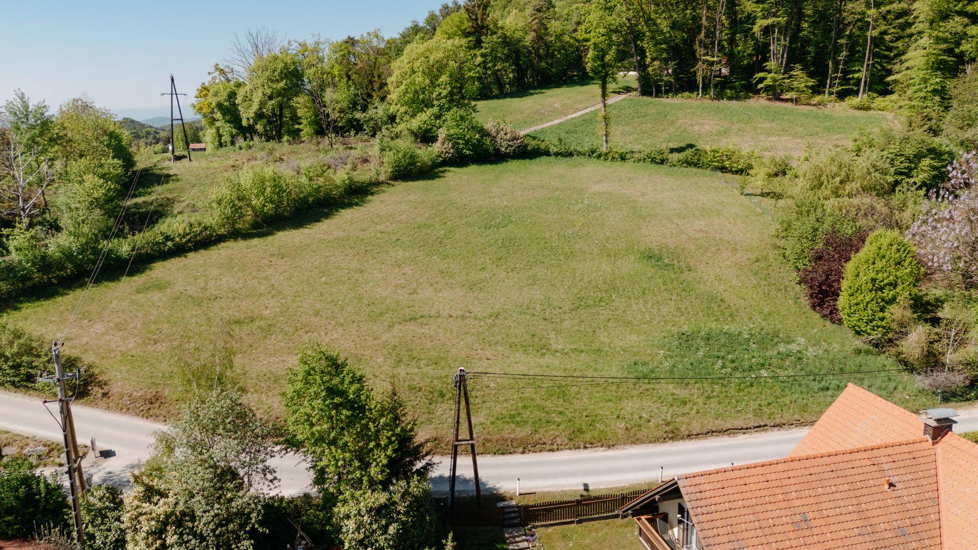 Luftaufnahme eines großen, offenen Grundstücks mit angrenzendem Wald und einer Landstraße im Vordergrund.