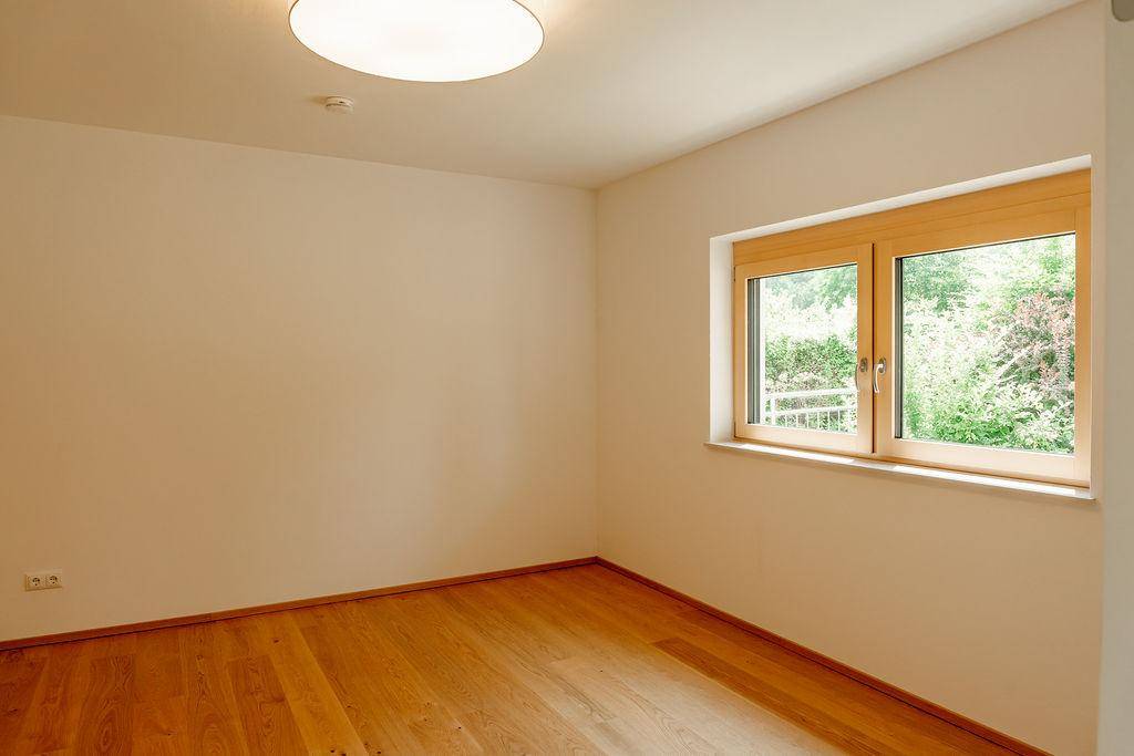 Helles Schlafzimmer mit Holzboden und großem Fenster, das viel Tageslicht hereinlässt.