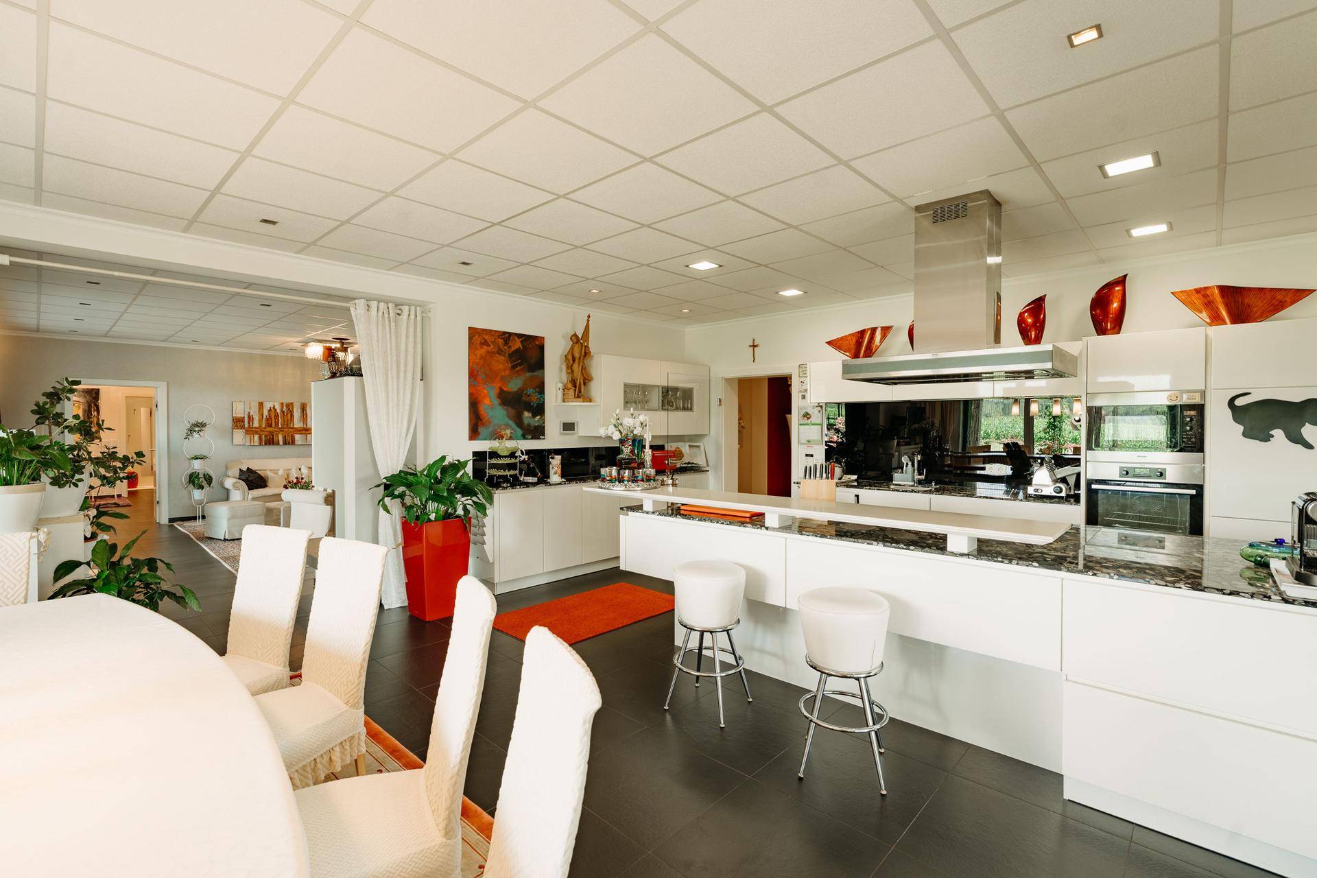 Moderne, offene Küche mit weißen Hochglanzfronten, Kücheninsel und Essbereich mit dunklem Fliesenboden.