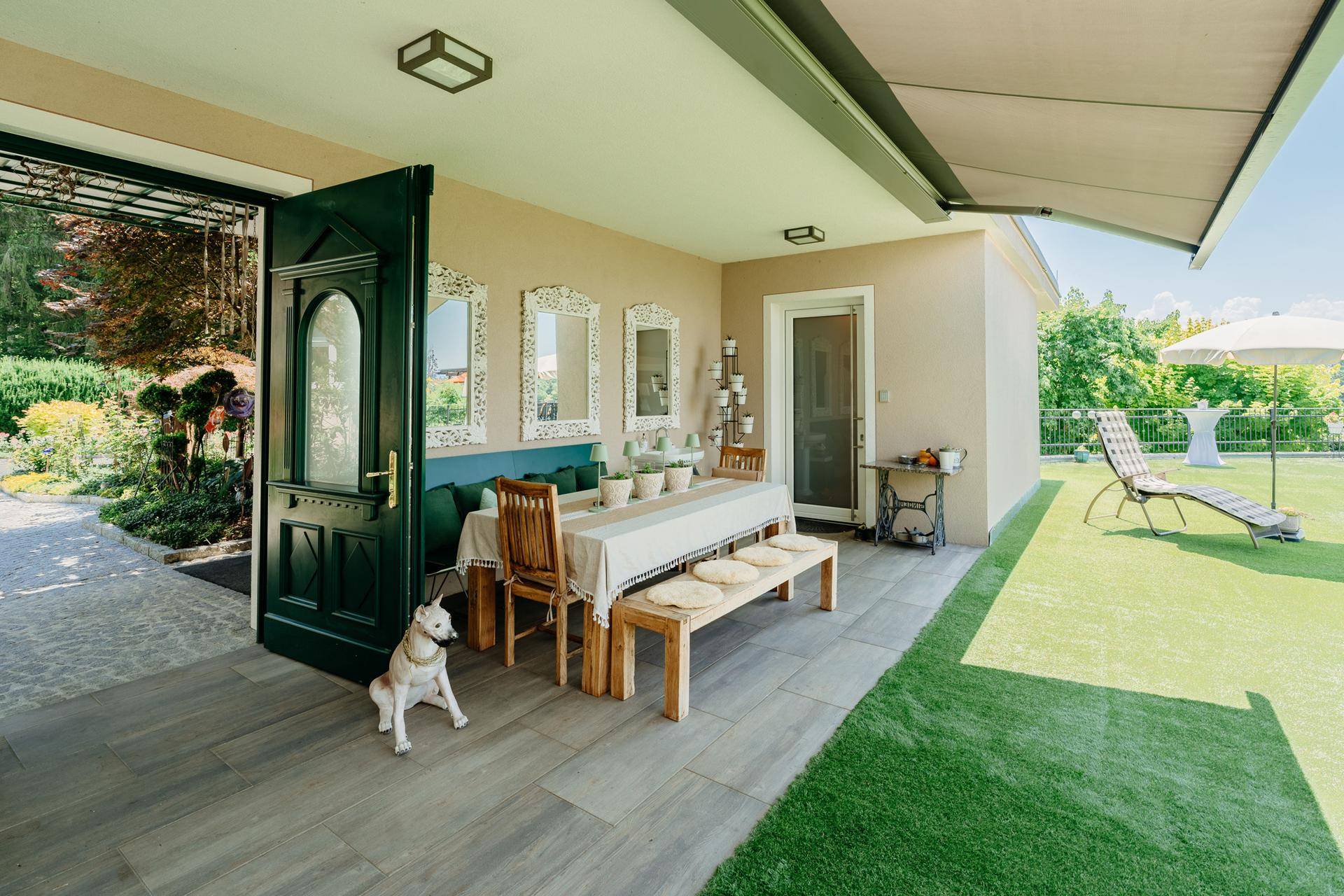 Überdachter Terrassenbereich mit Holztisch, Sitzbänken und Kunstrasen, ideal für entspannte Stunden im Freien.