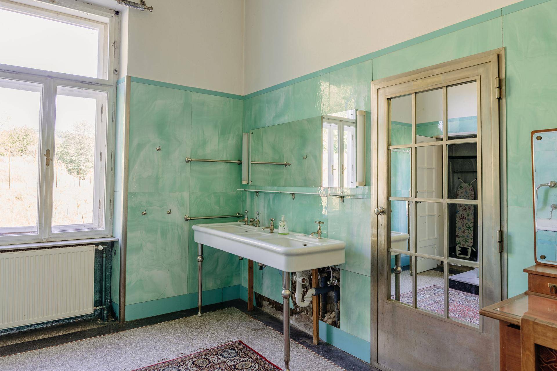 Geräumiges Badezimmer mit zwei Waschbecken, grünen Fliesen und großem Fenster.