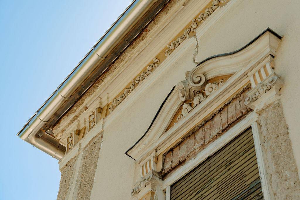 Detailaufnahme der historischen Fassade mit dekorativen Stuckelementen und Regenrinne.