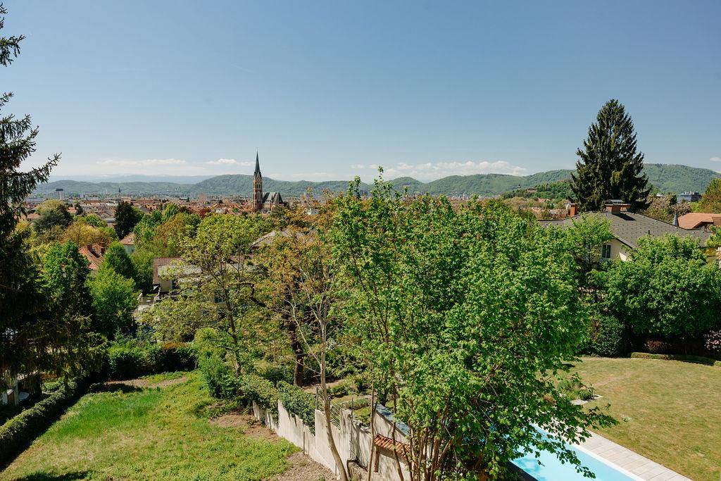 Gartenbereich mit Pool, üppiger Vegetation und Panoramablick auf die Stadt und Berge.