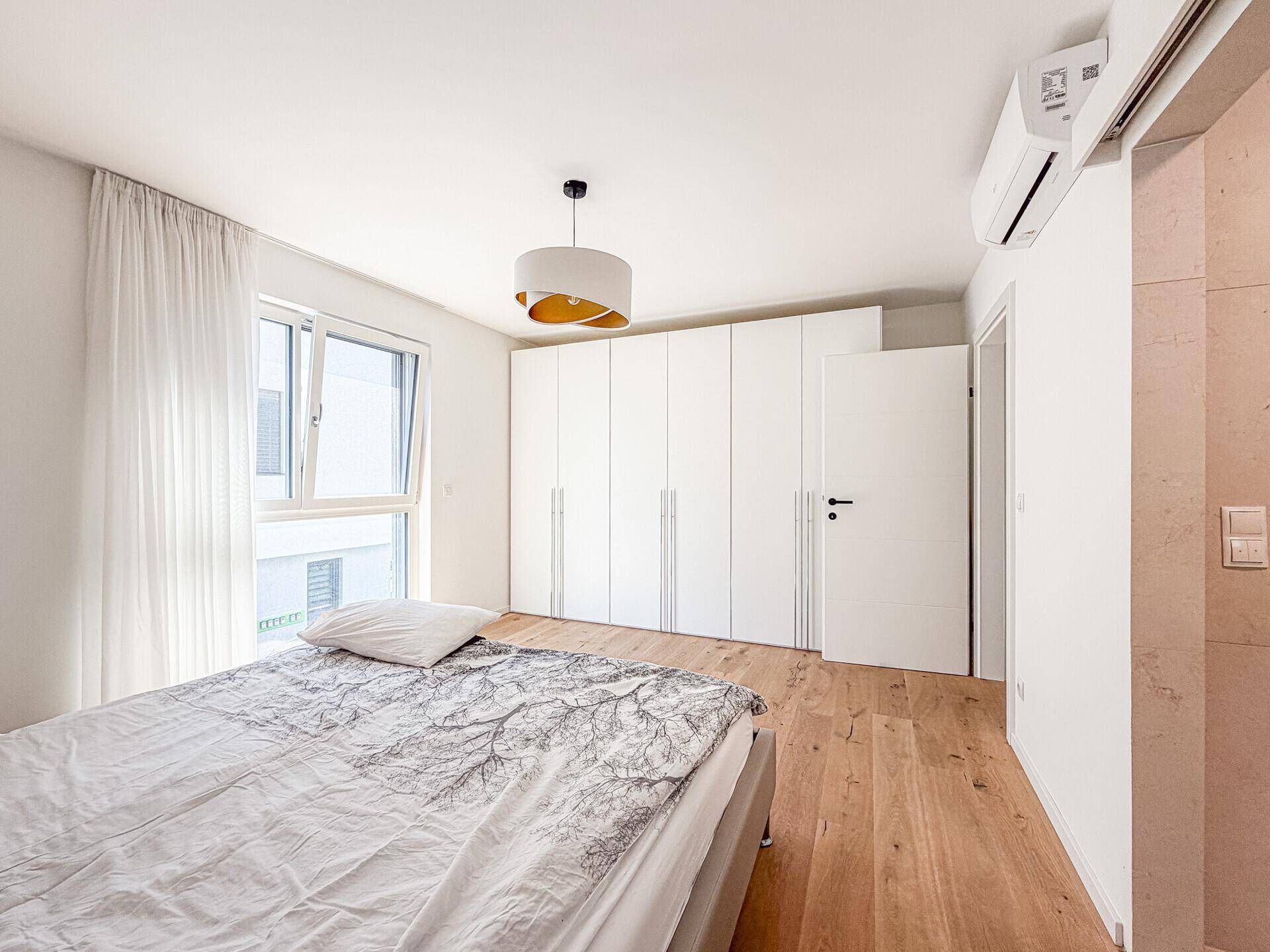 Schlafzimmer mit Holzboden, Einbauschränken, Klimaanlage und großem Fenster.
