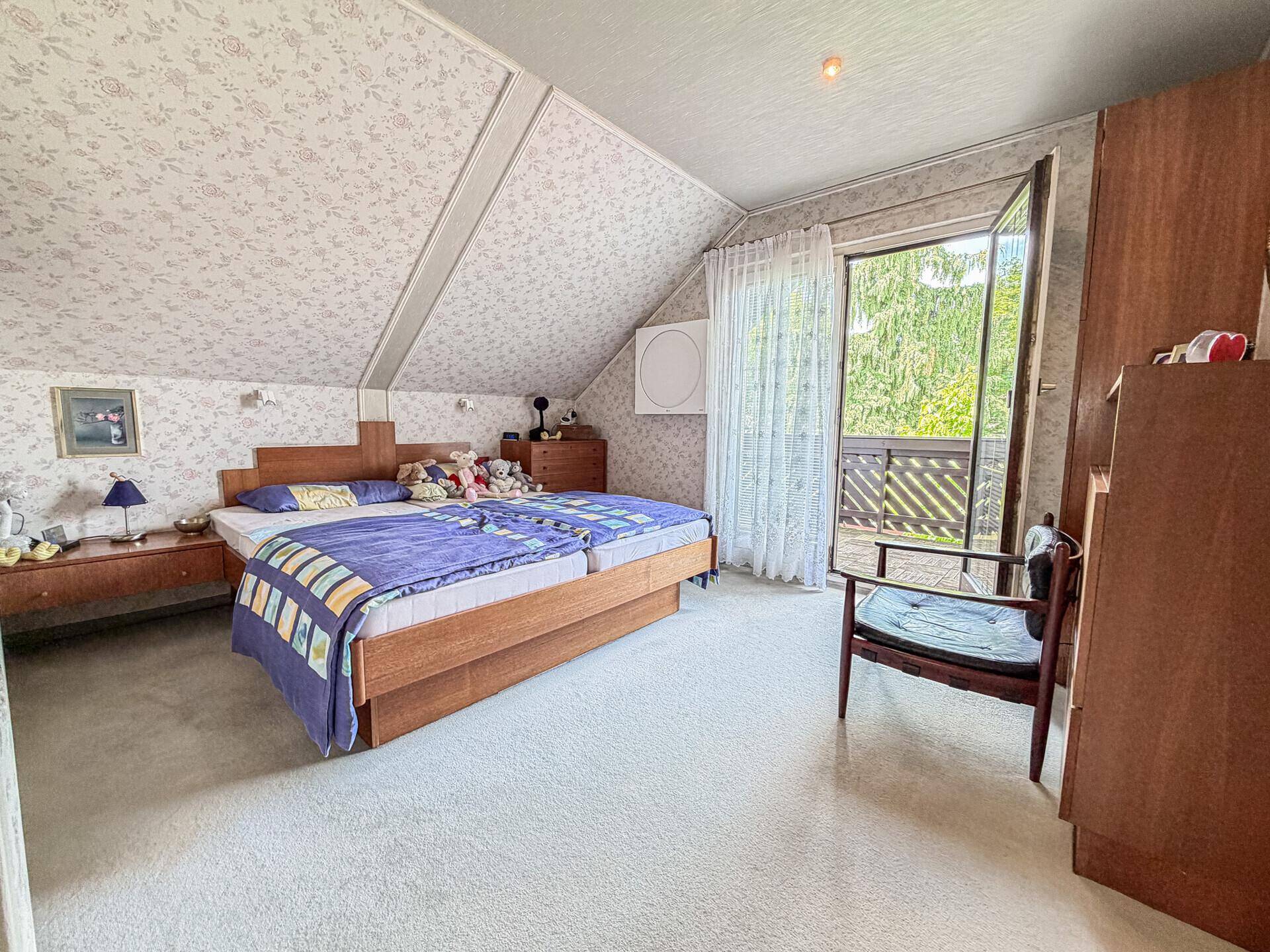 Schlafzimmer im Dachgeschoss mit Teppichboden, Doppelbett und Zugang zum Balkon.