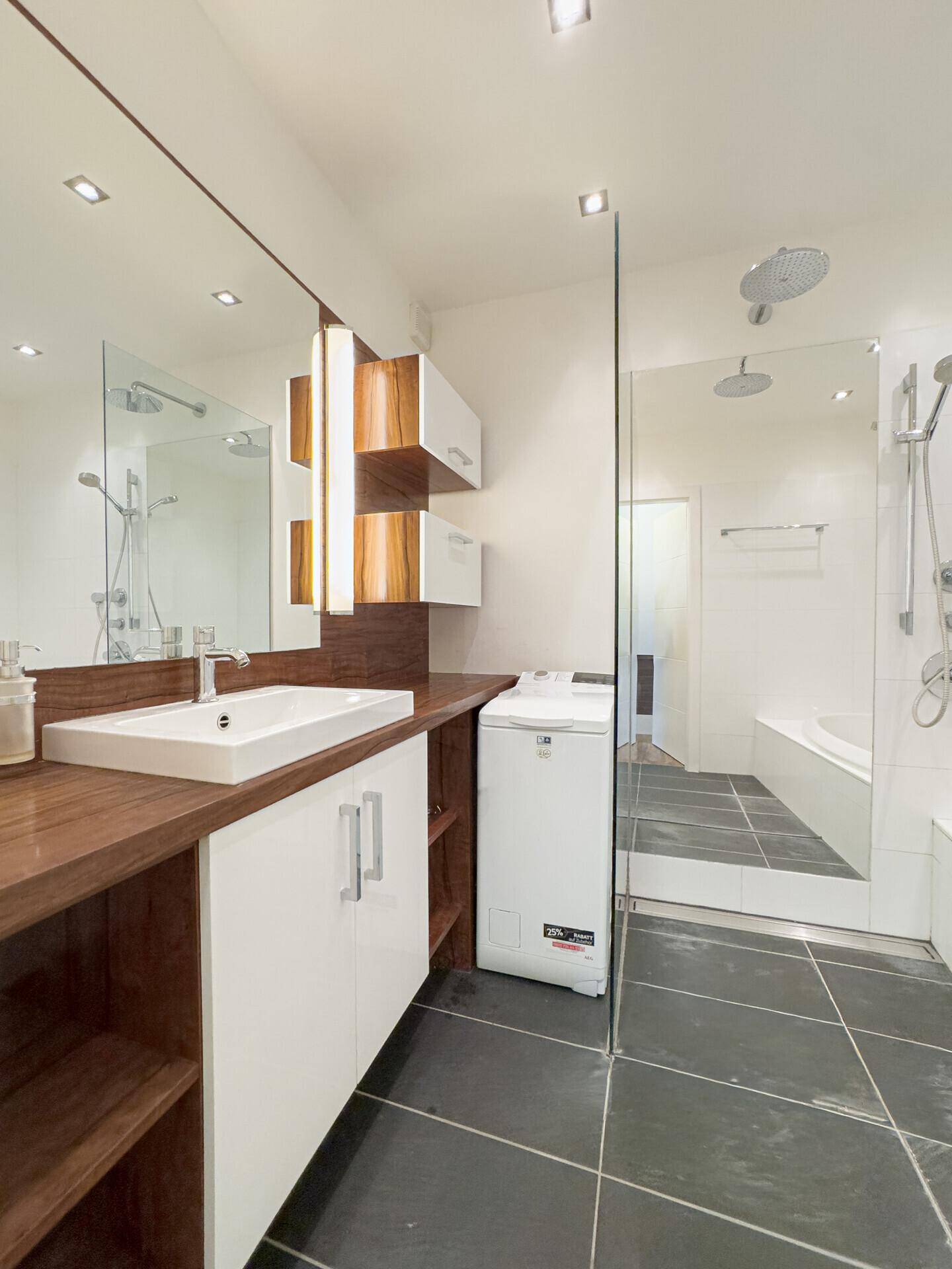 Elegantes Badezimmer mit Einzelwaschbecken, großem Spiegel und integrierter Waschmaschine.