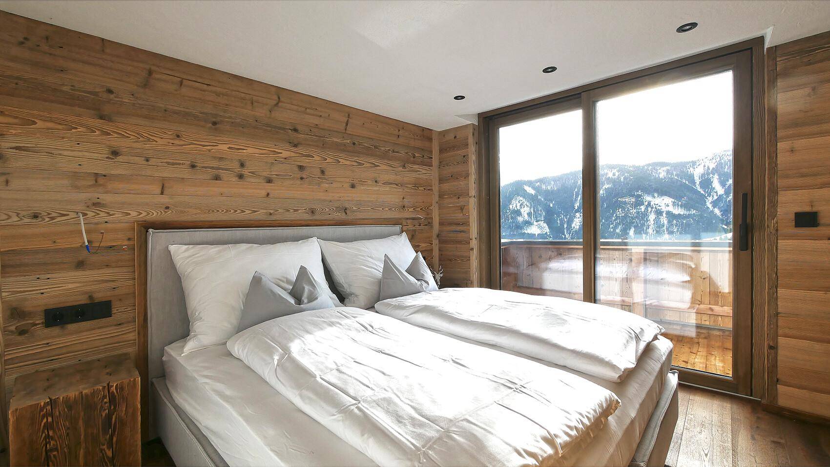 Helles Schlafzimmer mit Holzwänden, großem Fenster und direktem Zugang zu einem Balkon mit Bergblick.