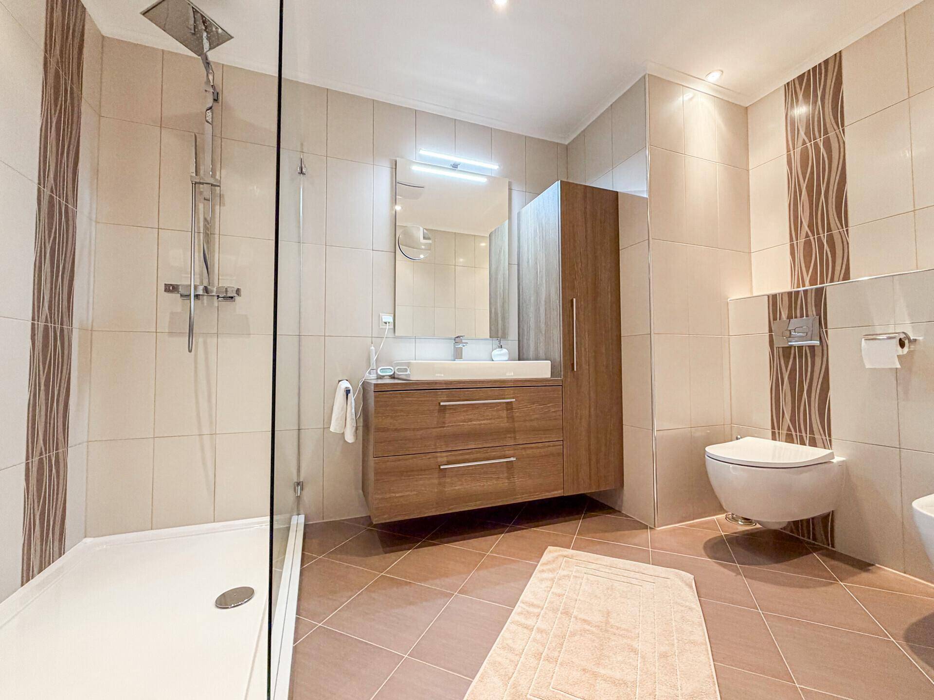 Modernes Badezimmer mit begehbarer Dusche, Waschtisch und Wand-WC in warmen Farbtönen.
