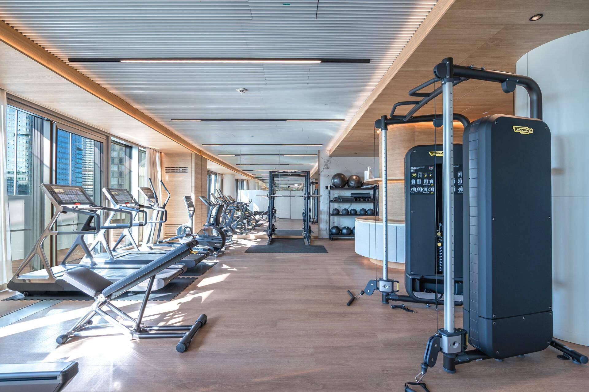 Gut ausgestatteter Fitnessraum mit modernen Trainingsgeräten und großen Fenstern für viel Tageslicht.