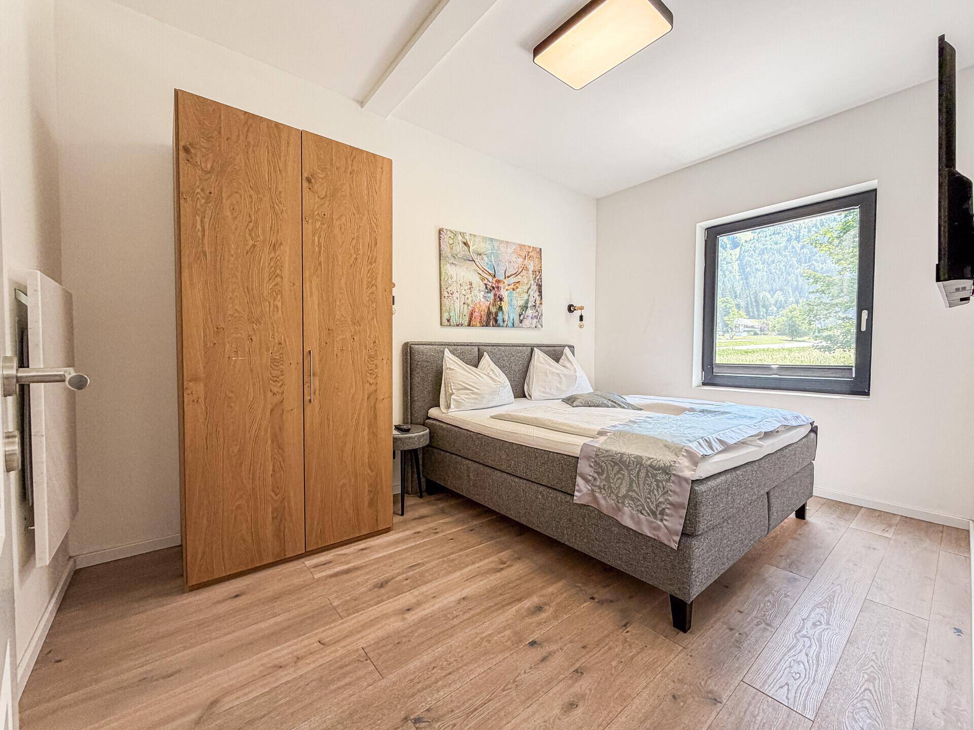 Helles Schlafzimmer mit Doppelbett, Holzschrank und Fenster mit Bergblick.