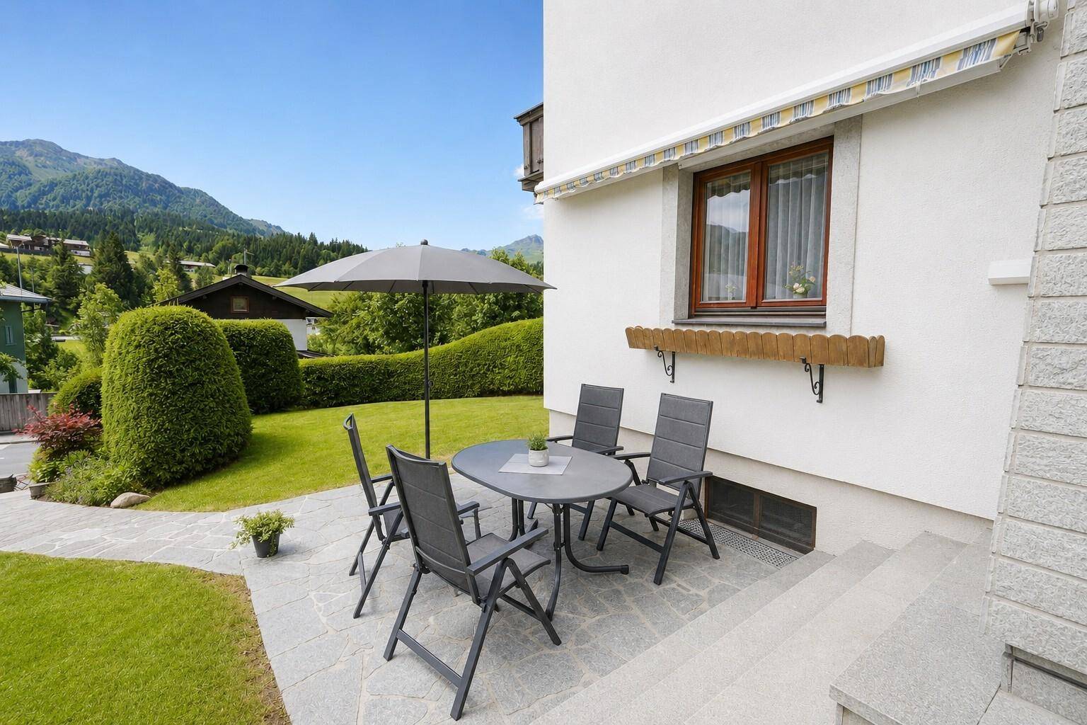 Sonniger Terrassenbereich mit Gartenmöbeln, Sonnenschirm und Blick auf die grüne Umgebung.