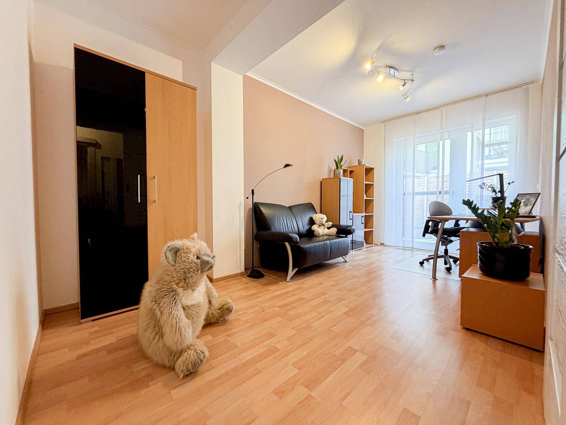 Vielseitiger Raum mit Sofa, Schreibtisch und hellem Holzboden, ideal als Wohn- oder Arbeitsbereich.