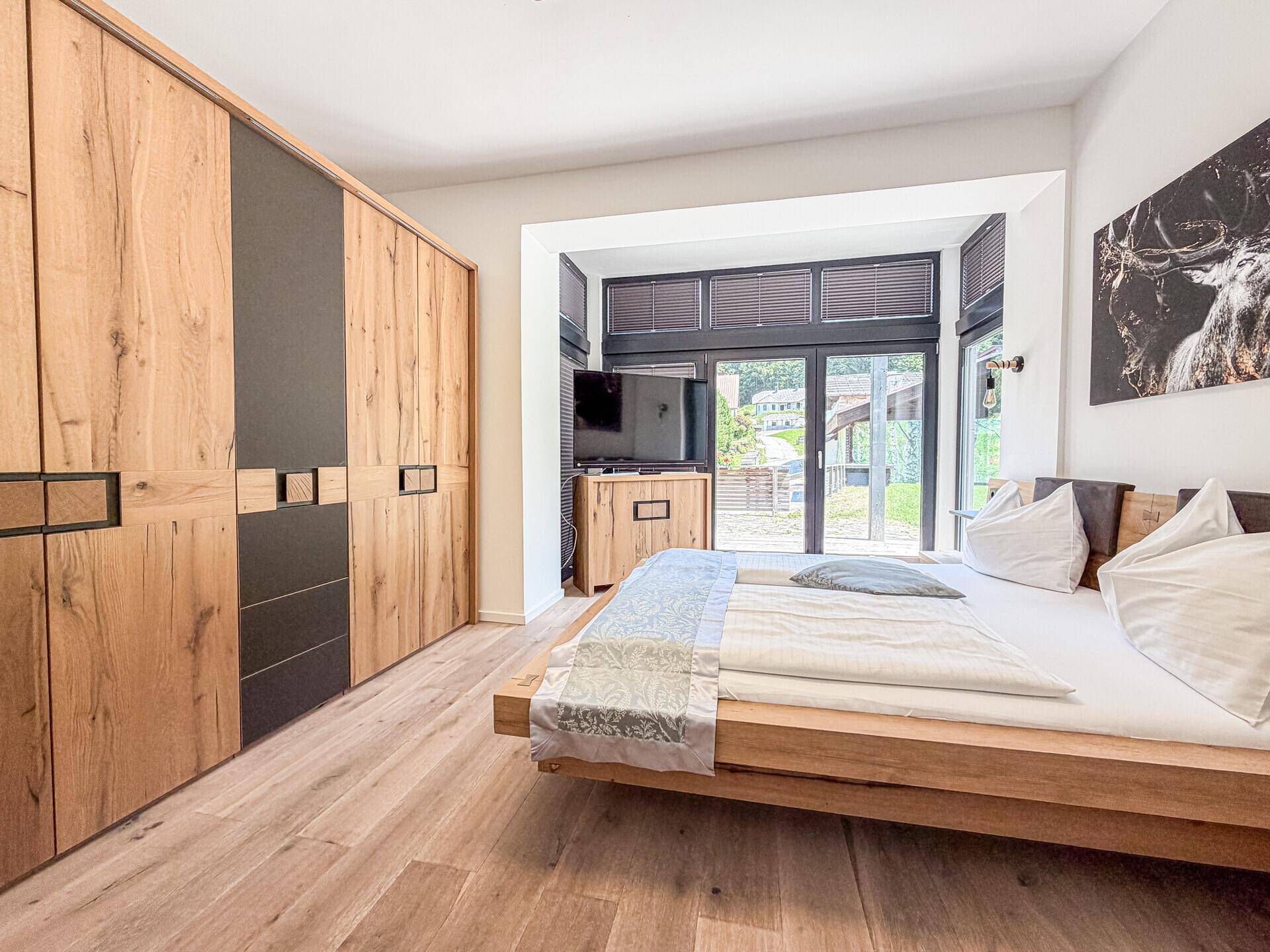 Schlafzimmer mit Holzbett, integrierten Schränken und großem Fenster mit Blick ins Grüne.