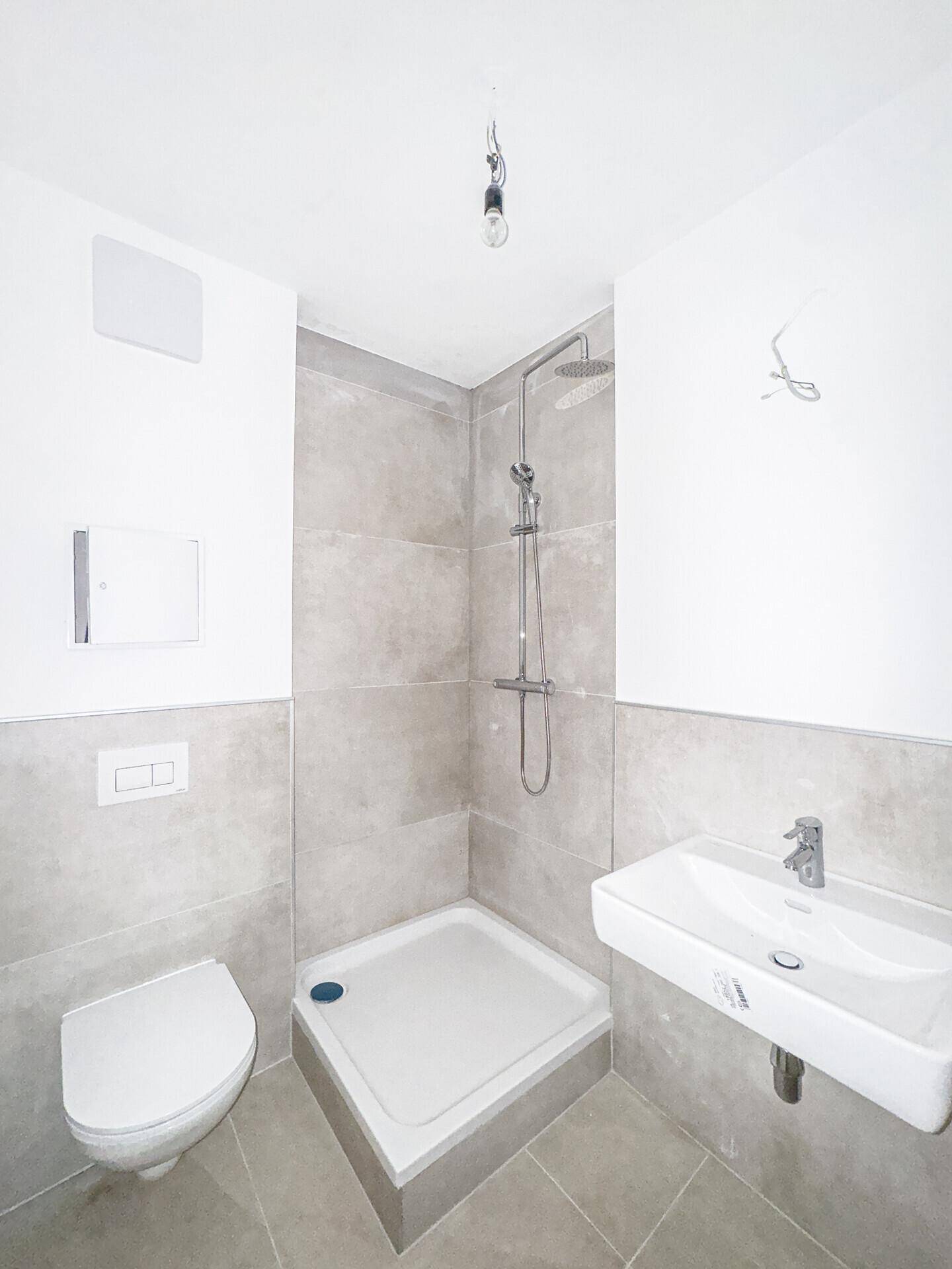 Modernes Badezimmer mit grauen Fliesen, Dusche, WC und Waschbecken.