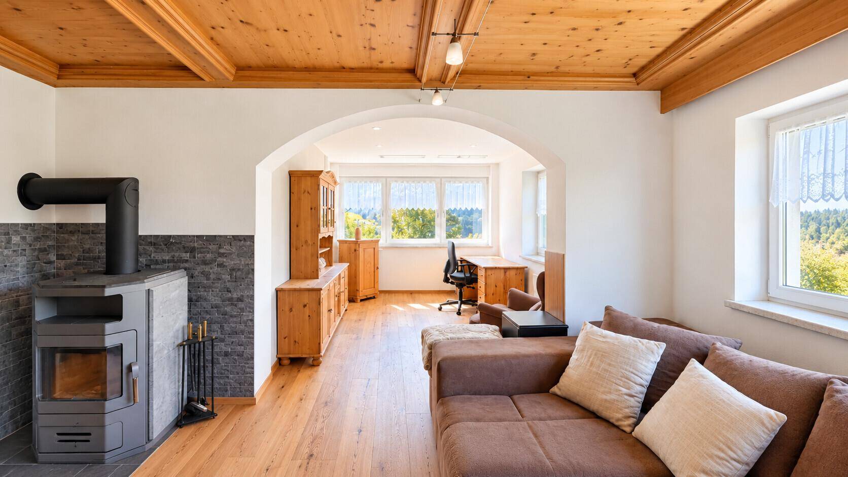 Gemütliches Wohnzimmer mit Holzbalkendecke, Kaminofen und angrenzendem Arbeitsbereich.