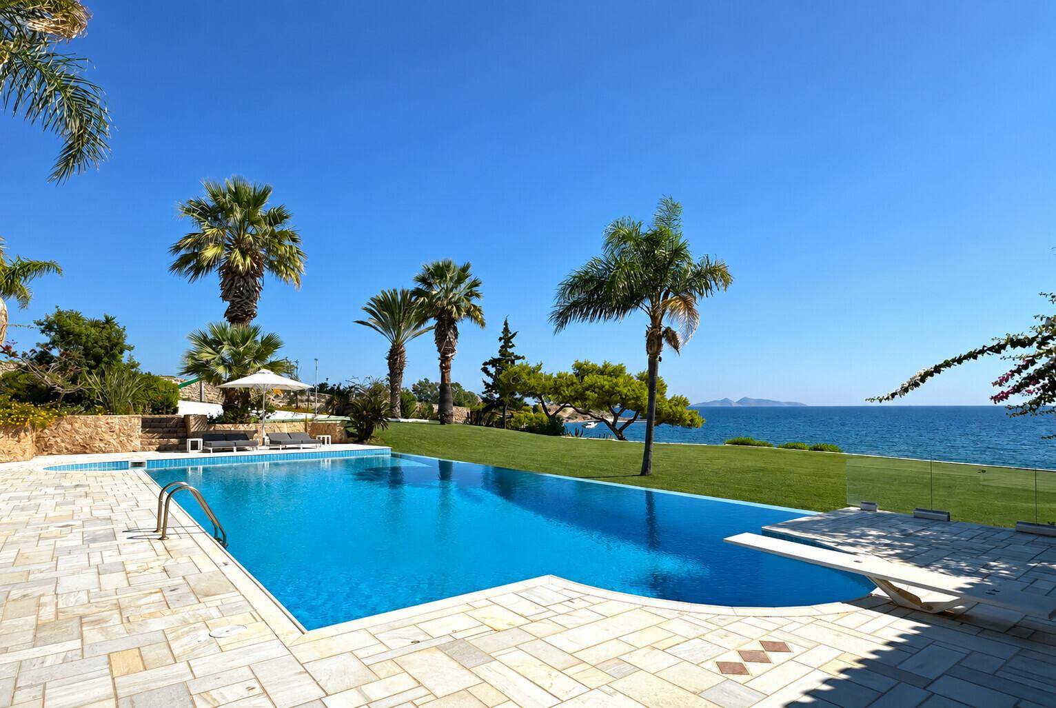 Großer Swimmingpool mit weitem Meerblick, umgeben von Palmen und einer sonnigen Terrasse.