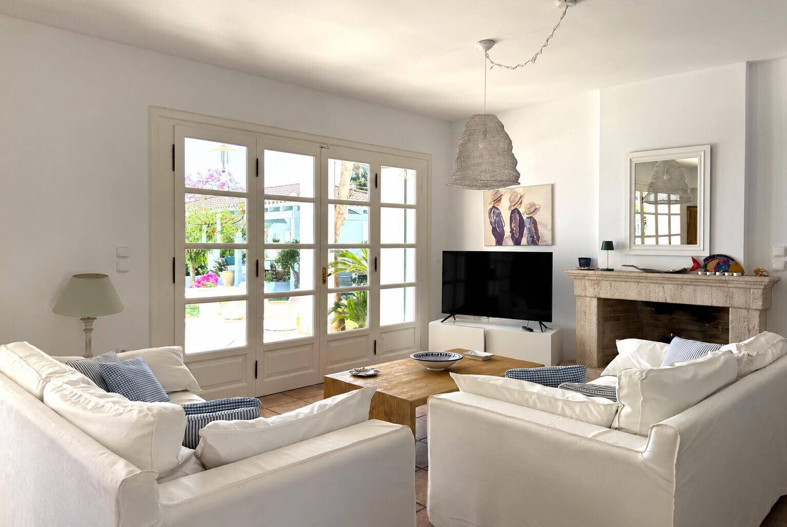 Helles Wohnzimmer mit gemütlichem Kamin, bequemen weißen Sofas und Zugang zur Terrasse.
