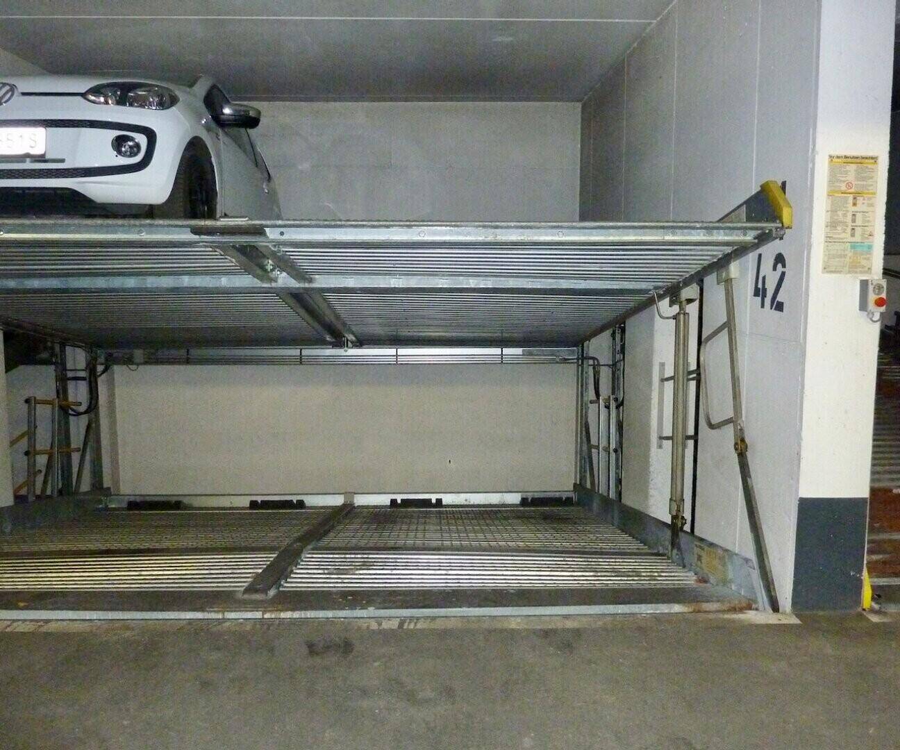 Ein Kleinwagen parkt auf der oberen Ebene eines doppelten Parklifts in einer modernen Tiefgarage.