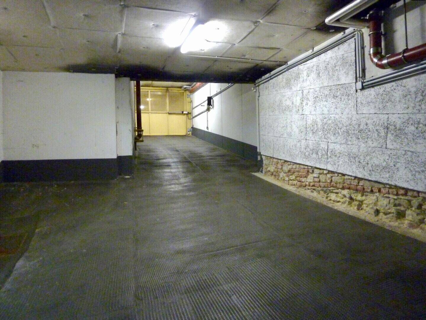 Ein Bereich der Tiefgarage mit sichtbaren Ziegelwänden, Betonboden und freiliegenden Rohren an der Decke.