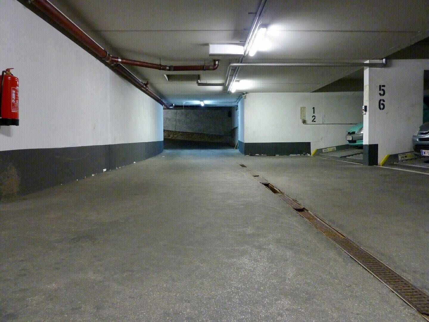 Einfahrt zu einer Tiefgarage mit einer Rampe und einem Feuerlöscher an der Wand, gut beleuchtet.