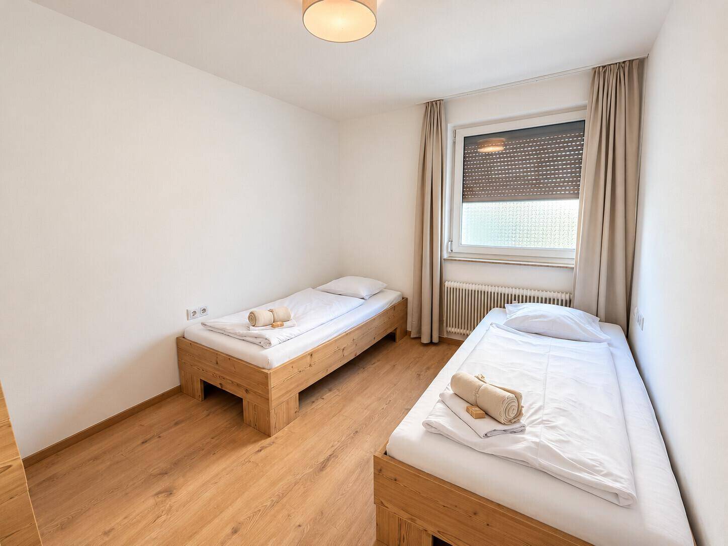 Helles Schlafzimmer mit zwei Einzelbetten aus Holz, Laminatboden und Fenster mit Rollladen.