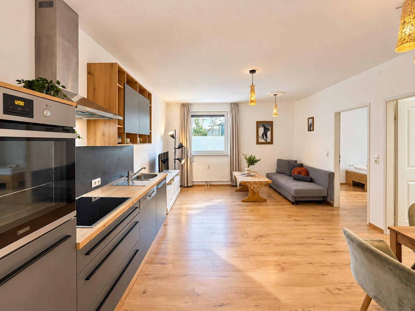 Offener Wohnbereich mit integrierter Küche, Sofa und Blick ins Grüne durch das Fenster.